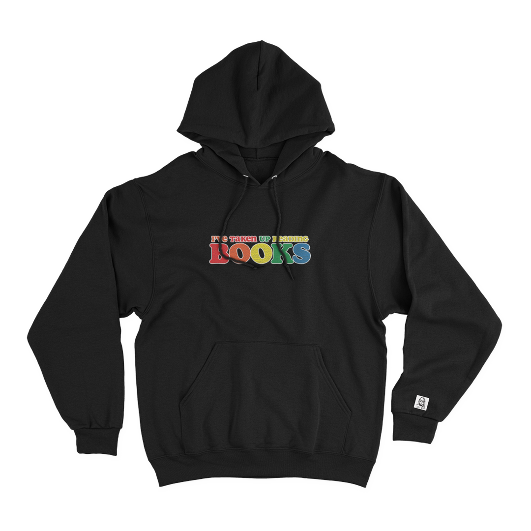 Black hoodie with a rainbow colored chenille patch on the front chest that reads "I've taken up reading books"